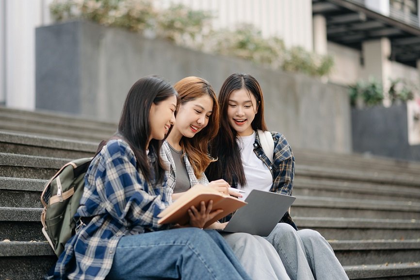 Three young Asian college students and a female student group work at the campus park in morning